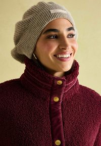 Beež ribaga kootud beanie sildiga; burgundia popline fliisjakk kõrge kaelusega ja kuldsete nuppudega.