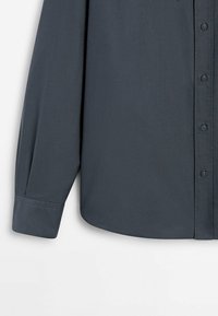 Camicia grigia scura con maniche lunghe, caratterizzata da una texture di tessuto liscia, un orlo dritto e un colletto standard.