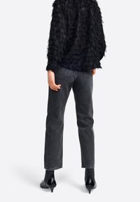 Sort tekstureret top med et fjerlignende design, parret med højtaljede mørkegrå jeans og skinnende sorte ankelstøvler med hæl.