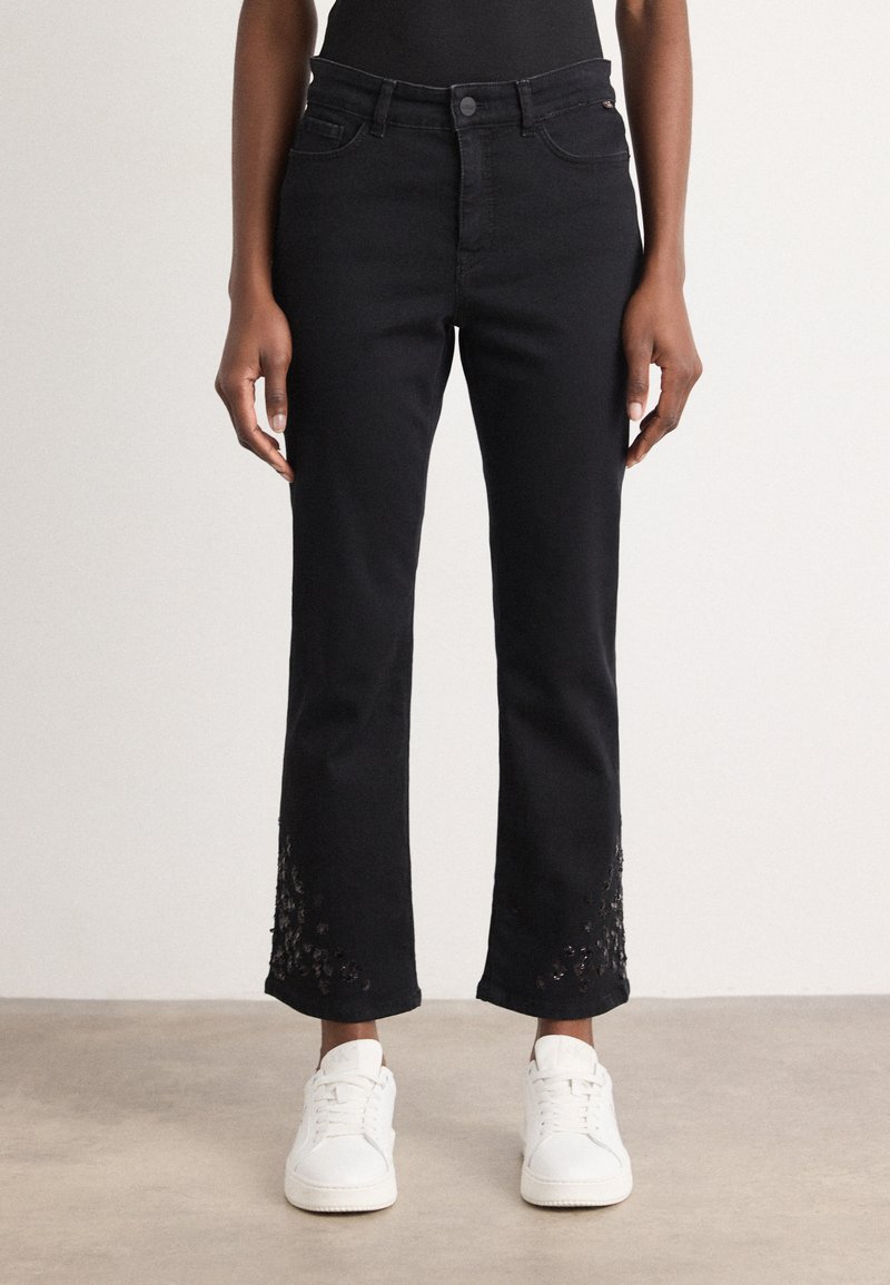 Jean en denim noir avec des jambes droites et des détails en dentelle à l'ourlet. Associé à des baskets blanches, design minimaliste sans effet usé.