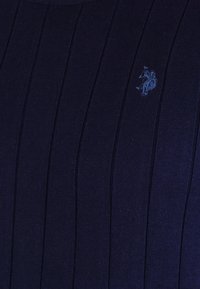 Marineblauwe ribstof met een klein geborduurd lichtblauw logo van een paard en ruiter.