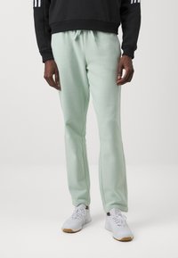 Calças de jogging verde-claro feitas de tecido macio, com um cós elástico e um cordão. Combinadas com sapatilhas de desporto brancas.