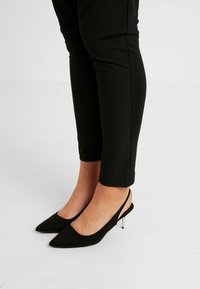 Black suede slingback heels with a pointed toe, featuring a sleek silver stiletto heel. Paired with black cropped trousers.