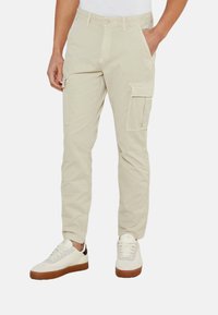 Pantalones cargo beige con dos bolsillos laterales, diseño de corte slim y material de algodón. Combinados con zapatillas blancas con suelas de goma marrón.