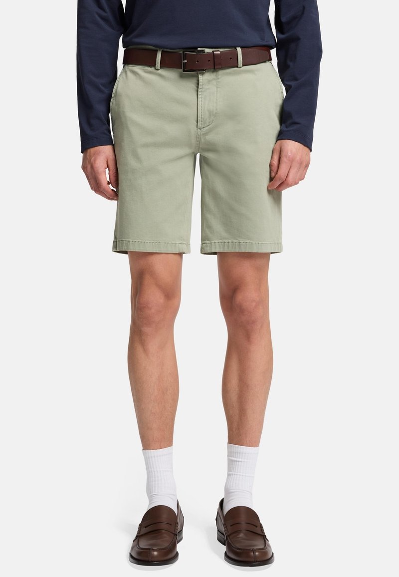 Lys grønne shorts lavet af bomuld, med lige snit, sidelommer og opkrøllede kanter, båret med et brunt bælte og brune sko.