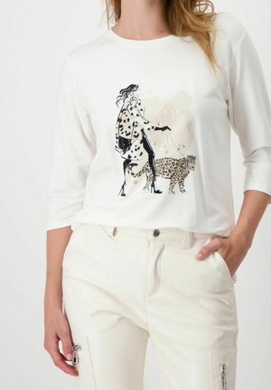Mujer con camisa blanca de manga larga con ilustración de una mujer elegantemente vestida paseando un leopardo con correa.