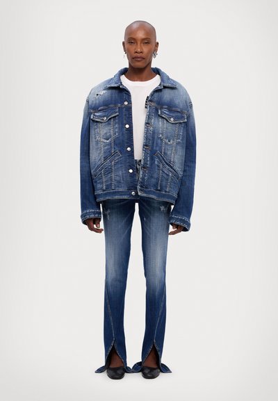 Oversized blue denim jacket with distressed details, paired with flared blue denim pants featuring split hems. White t-shirt underneath.