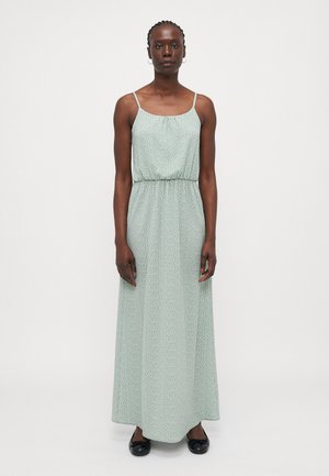 Vestido maxi de tela verde claro con un patrón de puntos, diseño sin mangas, cintura elástica y una falda fluida y texturizada. Combinado con bailarinas negras.