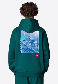 Sudadera en color azul verdoso con capucha, que presenta un gráfico del Monte Everest en la parte posterior, texto en negrita y un pequeño logotipo rojo en el lado inferior.