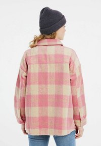 Chaqueta de franela de cuadros rosa y beige, de corte holgado, con cuello tipo solapa y mangas largas, fabricada en un suave tejido texturizado.