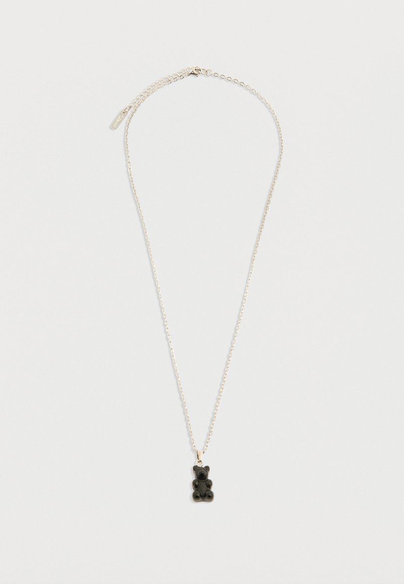 Ασημένιο κολιέ αλυσίδας με ένα μικρό μαύρο μενταγιόν σε σχήμα ζελέ αρκούδας σε απλό λευκό φόντο.