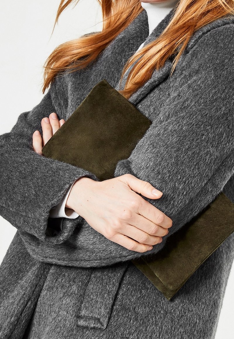 Grå ullkappa med strukturerad yta, håller en mörk olivgrön mockaväska. Detaljerad sömnad och rena linjer förhöjer designen.