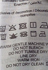 Care label with black text on a textured gray background, displaying care symbols and instructions for fabric washing and drying.