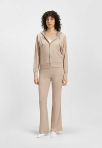 Beige katoenmengsel hoodie metrits en een trekkoord, gecombineerd met bijpassende flared broek. Gladde textuur met minimale accenten.