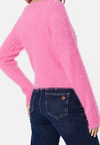 Fluffy, ribbed, pink sweater with long sleeves, featuring a soft texture. Paired with dark blue jeans with a brown label on the back pocket.
