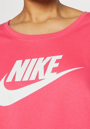 Person iført en lyserød T-shirt med rund hals og et stort hvidt Nike-logo og swoosh trykt på brystet.