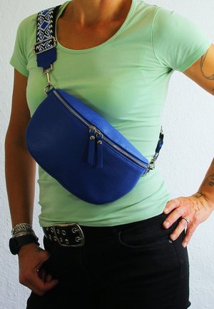 Blue leather crossbody bag with a textured finish, featuring a zippered top, tassel accents, and a patterned adjustable strap.