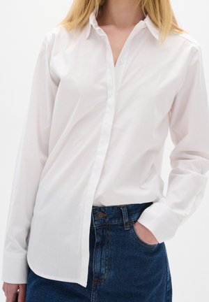 Bílá košile s dlouhým rukávem a límečkem, hladká textura a pečlivě složené manžety, zkombinováno s tmavě modrými džíny.