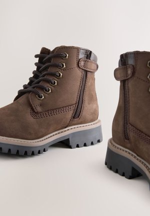 Bruine suède enkellaarsjes met veters en rits, rubberen profielzolen en contrasterende leren accenten. Gestikte details aan de zijkanten.