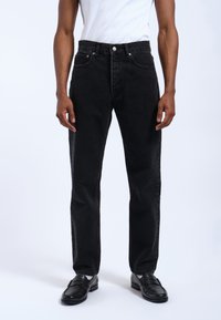 Jeans de mezclilla negros con corte recto, diseño de cinco bolsillos, herrajes plateados y detalles de costura mínimos, combinados con mocasines negros.