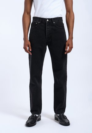 Jeans de mezclilla negros con corte recto, diseño de cinco bolsillos, herrajes plateados y detalles de costura mínimos, combinados con mocasines negros.