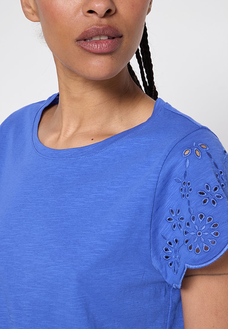 Blå kortärmad topp i mjukt tyg. Utrustad med dekorativa broderade blommönster på ärmarna och en rundad krage.