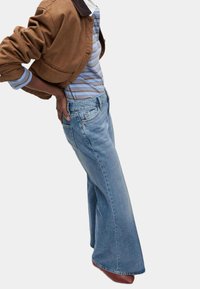 Jasnoniebieskie szerokie dżinsy wykonane z denimu, z klasycznym pięcioma kieszeniami i subtelnymi detalami przeszyć. Połączone z pasiastą bluzką i brązową kurtką.