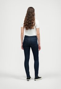 Tight jeans i mørkeblå denim, høy midje med en jevn tekstur. Har klassiske baklommer og sømdetaljer. Matchet med svarte joggesko.