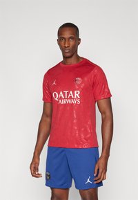 Punane spordivormi särk, millel on tooni trükk, "QATAR AIRWAYS" logo ja Jordani brändimine; koos siniste lühikestega ja logo aktsentidega.