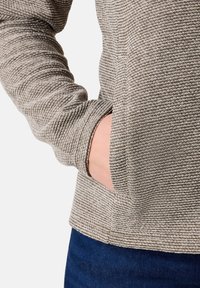 Maglione beige strutturato con design a coste, dotato di una tasca laterale e polsini aderenti. Il tessuto ha un aspetto morbido e tessuto.