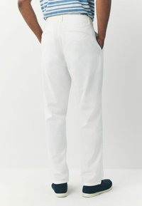 Valged sirge lõikega püksid tagataskutega, kantud tumesiniste slip-on kingadega, mis näitavad siledat kangatekstuuri.