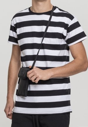 Personne portant un t-shirt rayé noir et blanc tenant un petit sac bandoulière noir avec une sangle traversant la poitrine.