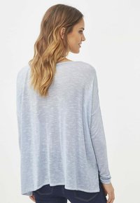 Top de punto de manga larga en azul claro, con un corte holgado. Presenta una textura suave, escote ancho, dobladillo trasero más largo y una tela ligeramente transparente.