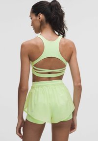 Neon sárga sportmelltartó keresztpántos kialakítással és kivágott részletekkel, amely a hozzá illő rövidnadrággal van párosítva, amely rugalmas derékpánttal és réteges szegéllyel rendelkezik.