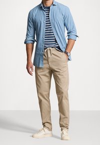 Vaaleansininen chambray-paita tummansinisen ja valkoisen raidallisen t-paidan päällä, yhdistetty beigeihin naruvöihin ja kermaisiiin tennareihin. Yksinkertainen muotoilu.