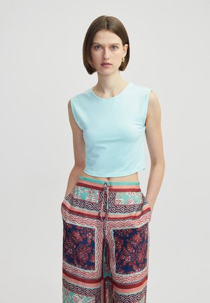 Lichtblauw mouwloos crop-top gemaakt van rekbaar materiaal, gecombineerd met wijde broek met patronen in bloemige en geometrische ontwerpen.
