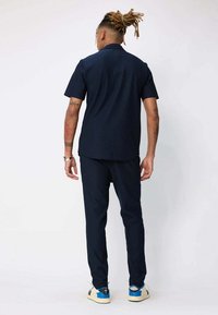 Chemise à manches courtes bleu marine et pantalon tapered en tissu léger, avec un design épuré et une texture subtile. Des baskets blanches et bleues viennent compléter le look.