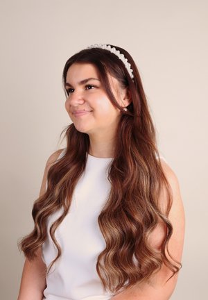 Fascia con perle su lunghi capelli mossi castani, indossata con una canotta bianca senza maniche, su uno sfondo neutro. Design semplice ed elegante.