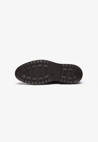 Suela de zapato de goma negra que presenta un agarre texturizado, forma contorneada y un dibujo en relieve con surcos profundos para mayor tracción.