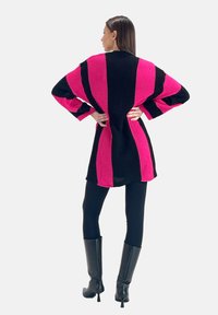 Overmaat gebreide trui met gedurfde roze en zwarte strepen, een ontspannen pasvorm en lange mouwen. Gecombineerd met zwarte leggings en kniehooge laarzen.