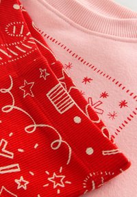 Twee textielstukken: een rood corduroy-stof met witte patronen, waaronder sterren en krullen, naast een zacht roze stof met vergelijkbare prints.