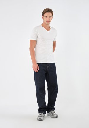 Weißes Baumwoll-V-Ausschnitt-T-Shirt kombiniert mit dunkelblauen Denim-Jeans. Verfügt über ein gerades Bein Design und silberne Sportschuhe mit reflektierenden Akzenten.