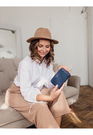 Navy blue wallet with a patterned texture, rectangular shape, and zip closure, held by a person wearing a white shirt and beige pants.