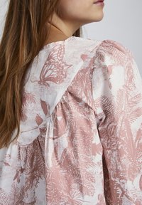 Lett, mønstret bluse med et pink og hvidt botanisk design, detaljer med samlet ryg og blødt, svævende stof.