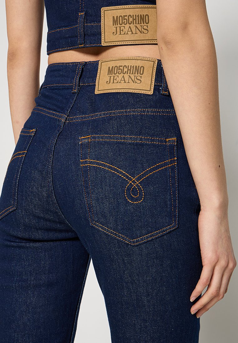 Granatowe dżinsy z pomarańczowymi szwami, posiadające dwie widoczne skórzane metki oraz zakrzywiony wzór na tylnej kieszeni.