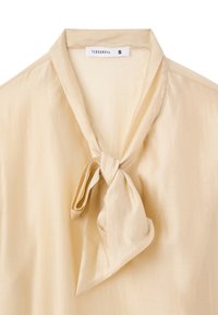 Blusa color crema con una morbida texture di satin, dotata di un colletto annodato all' altezza del collo. L'etichetta riporta la scritta "Terranova" e la taglia "S."