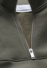 Felpa verde in pile con zip argentata, collo a costine e un'etichetta all'interno del colletto con la dicitura "ARMEDANGELS."