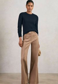 Maglione a maglia blu scuro con polsini a costine abbinato a pantaloni larghi color marrone chiaro a vita alta, dotati di tasche frontali e cuciture a contrasto.