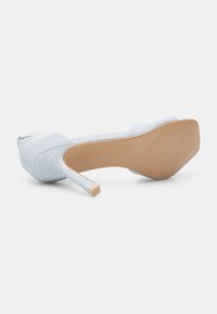 Korkokenkä, jossa on vaaleansininen kiiltävä päällinen, suljettu varvas ja beige synteettinen pohja. Ominaisuuksiin kuuluu sulava siluetti ja terävä korko.