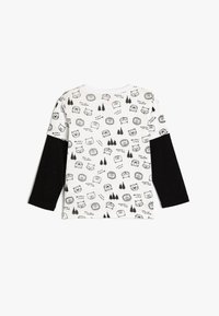 Langarm-T-Shirt mit einem weißen Körper, verziert mit schwarzen Tier- und Naturmotiven, kontrastiert mit einfarbigen schwarzen Ärmeln.